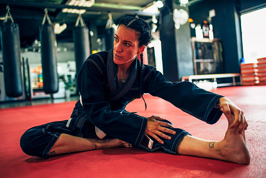 Woman in black karategi stretching her legs in a training gym, Sporty woman in black kimono practicing leg stretching before starting karate fight in the gym. Photograph by Jose Luis  Agudo Gonzalez
