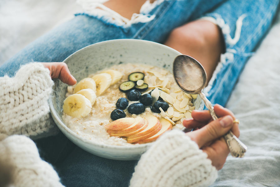 Woman in jeans and sweater eating healthy oatmeal porriage Photograph by Foxys_forest_manufacture