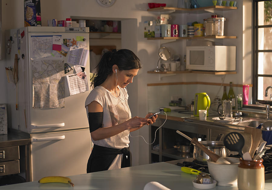 Woman in kitchen preparing music for a run Photograph by 10000 Hours