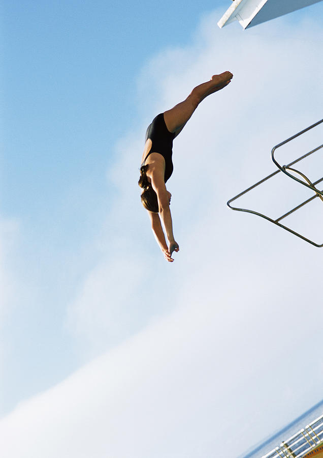 Woman in mid-dive, low angle view, full length, blue sky in background. Photograph by Teo Lannie