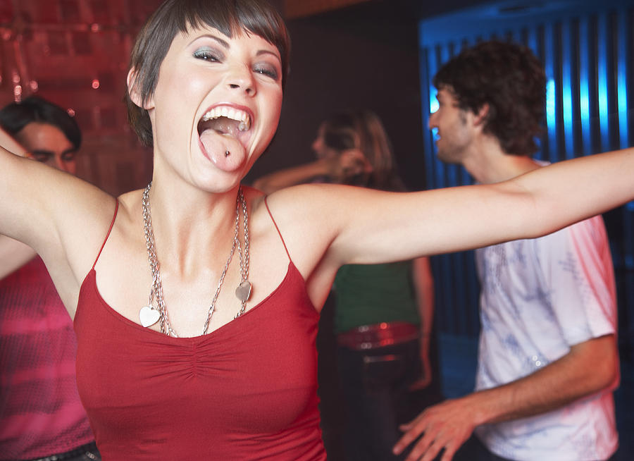 Woman in nightclub sticking her tongue out with people dancing behind her smiling Photograph by Paul Bradbury