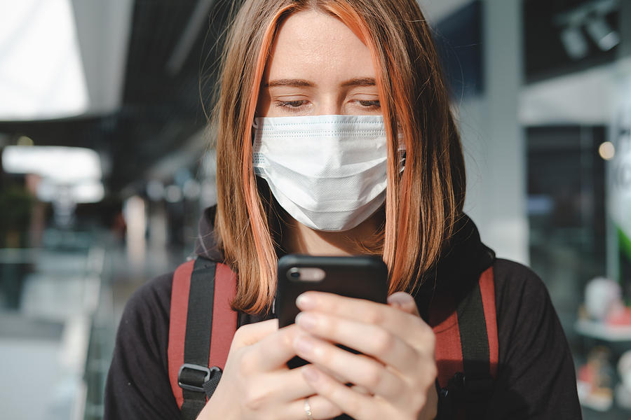 Woman in protective face mask using the phone at a public place. Photograph by Photoboyko