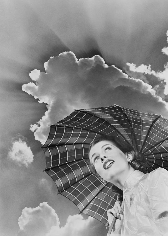 Woman in raincoat holding umbrella looking up into sky of dark clouds and impending storm. Photograph by H. Armstrong Roberts