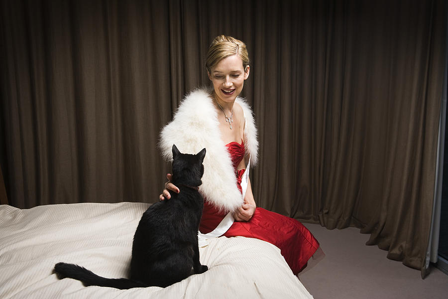 Woman in red dress stroking cat on bed, smiling Photograph by Betsie Van der Meer