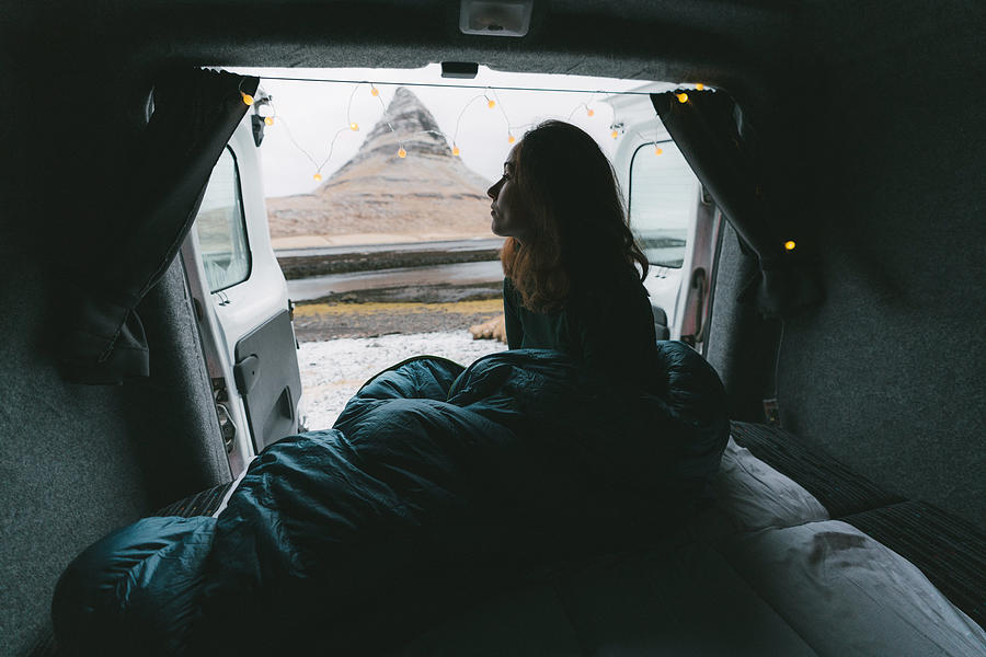 Woman in sleeping bag looking at Kirkjufell mountain from camper van Photograph by Oleh_Slobodeniuk