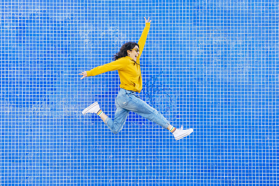 Woman jumping in front of a blue background Photograph by Karrastock