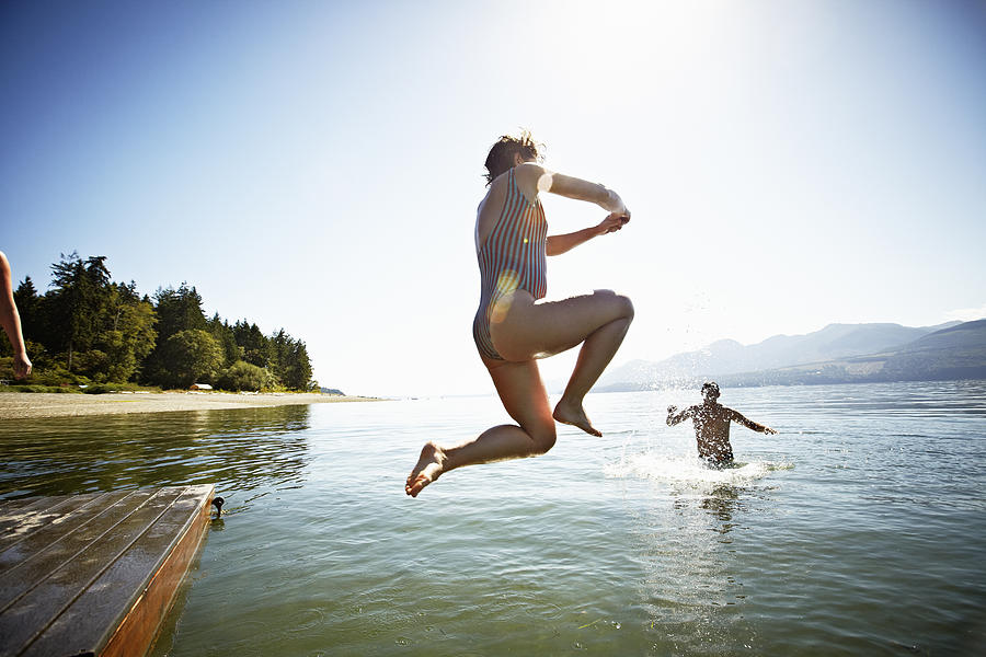 Woman jumping off of floating dock into water Photograph by Thomas Barwick