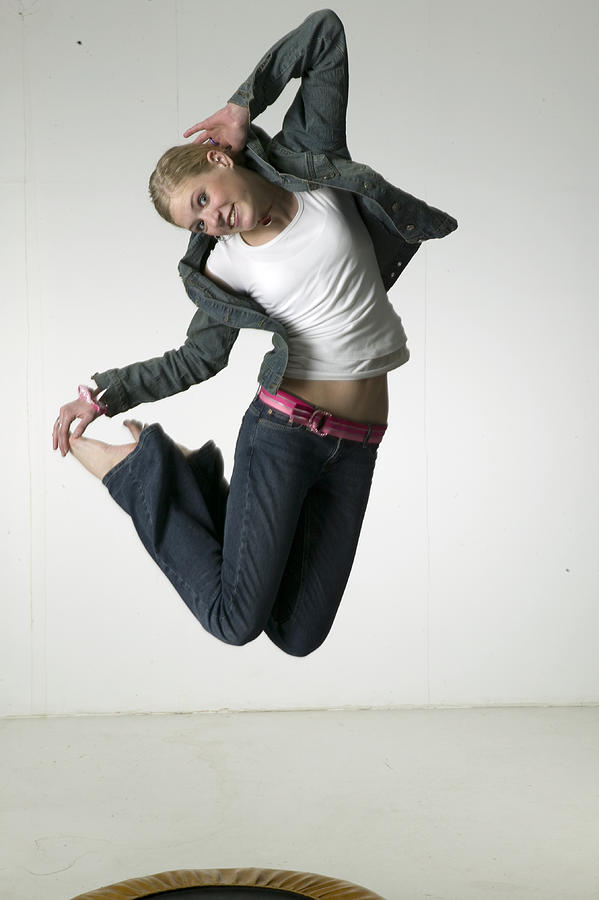 Woman jumping on trampoline in studio Photograph by Photodisc