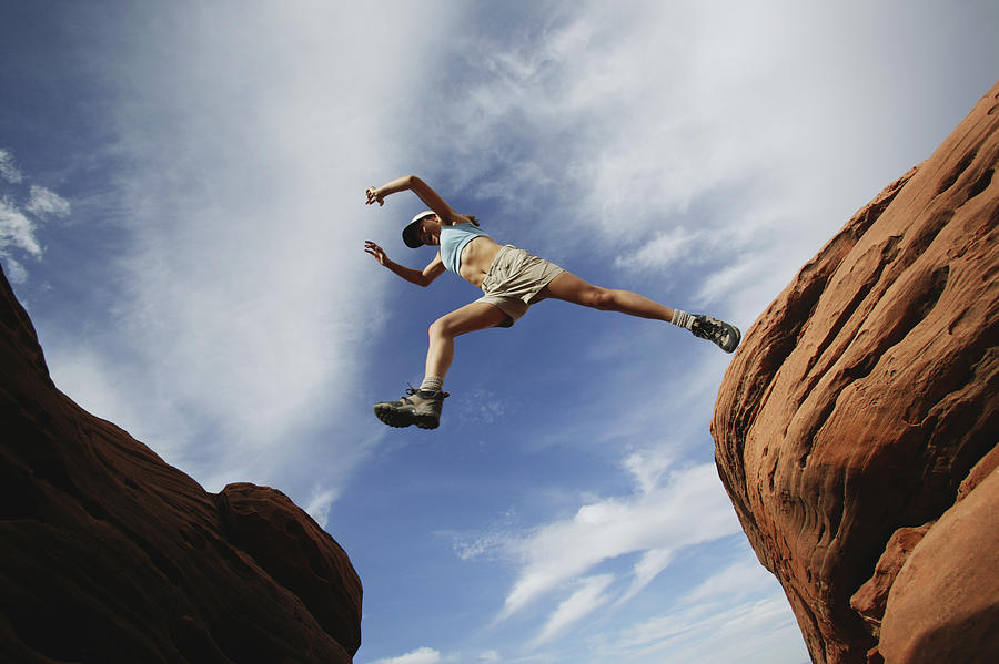 Woman jumping over rock ledge Photograph by Jupiterimages