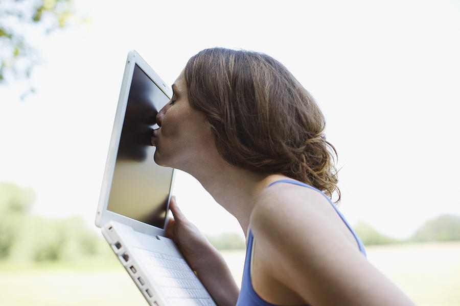 Woman kissing laptop screen outdoors Photograph by Tom Merton