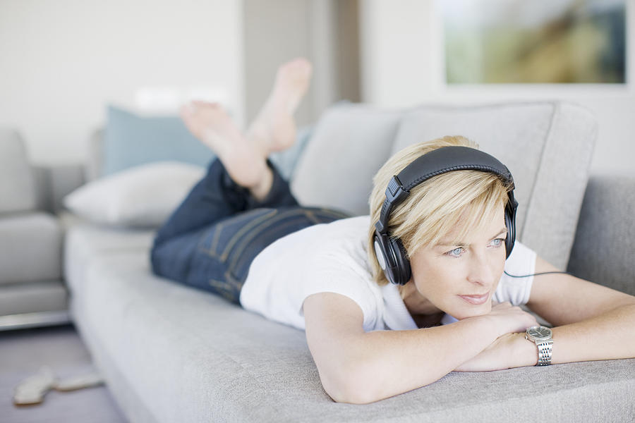 Woman listening to headphones in living room Photograph by Paul Bradbury
