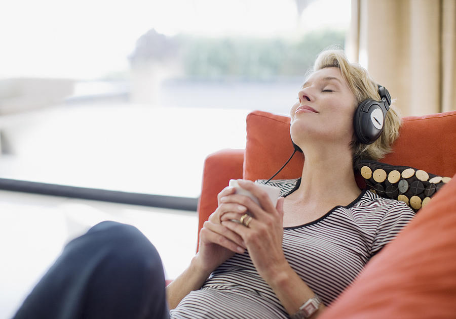 Woman listening to headphones on sofa Photograph by Paul Bradbury