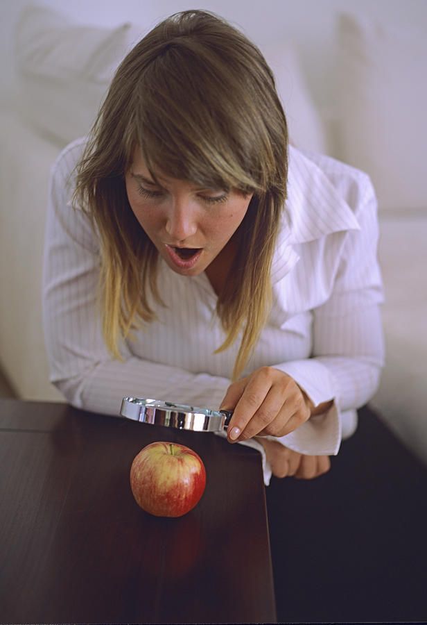 Woman looking at apple through magnifying glass Photograph by Daniel Krolls
