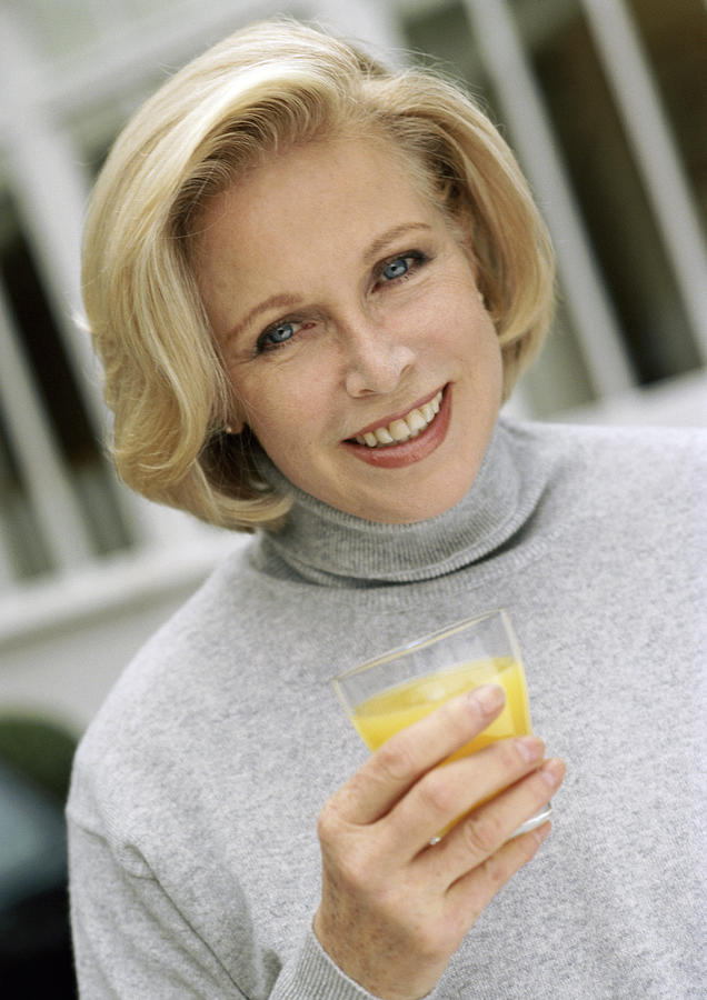 Woman looking at camera holding glass of orange juice, close up, portrait. Photograph by Eric Audras