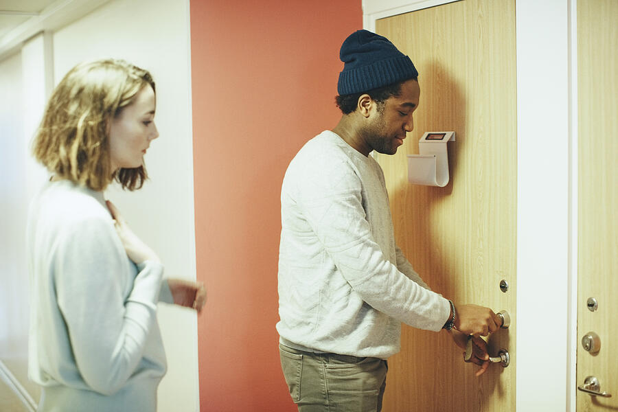 Woman looking at male friend opening door lock in college dorm Photograph by Maskot