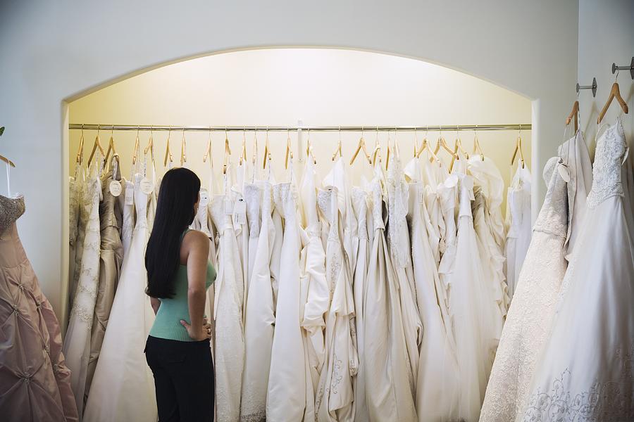 Woman looking at wedding dresses on rack Photograph by Terry Vine