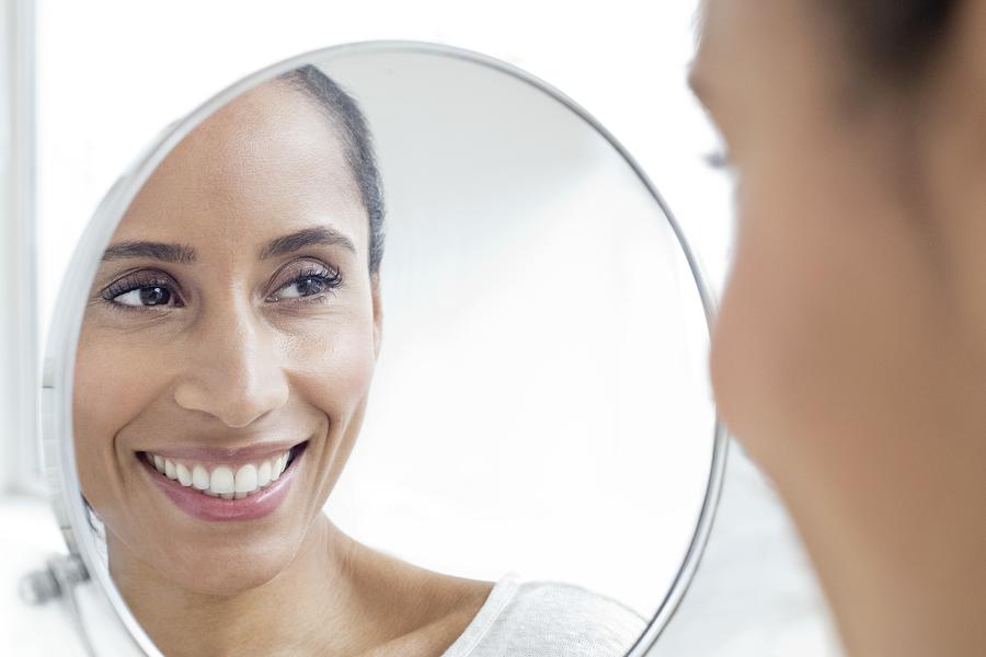 Woman looking in mirror, smiling Photograph by Science Photo Library