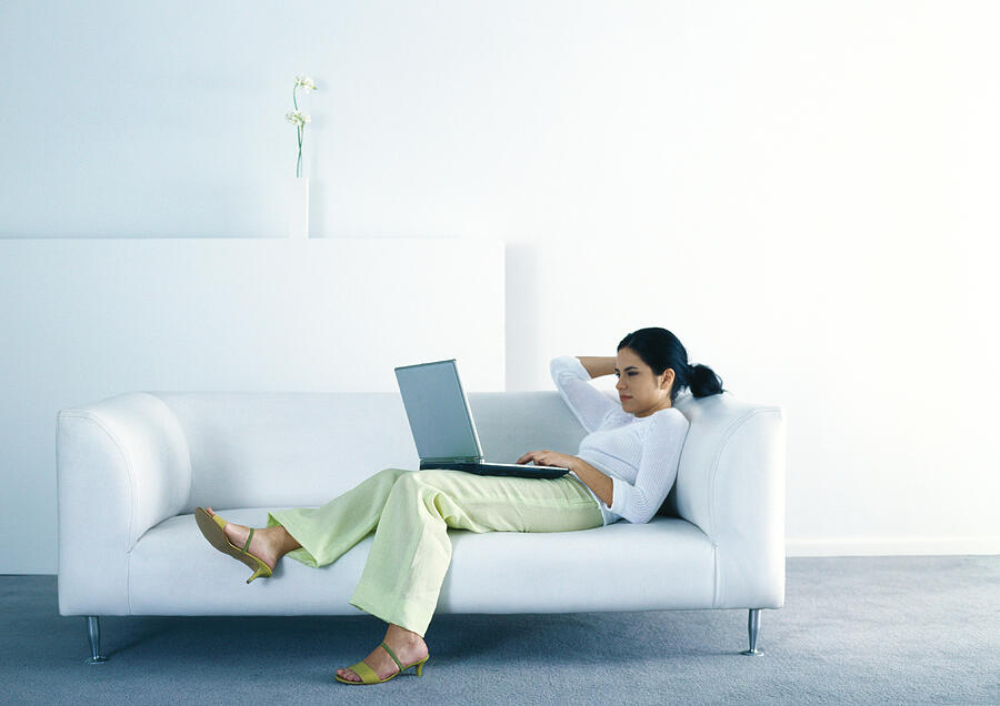 Woman lounging on sofa and using laptop Photograph by Laurence Mouton