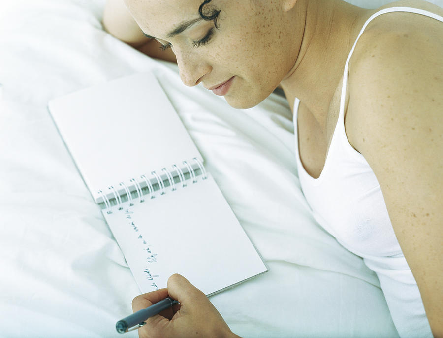 Woman lying on side on bed writing in notebook with pen Photograph by Laurence Mouton