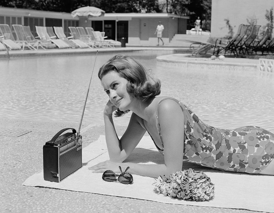 Woman lying on towel poolside listening to radio with antenna up. Photograph by H. Armstrong Roberts