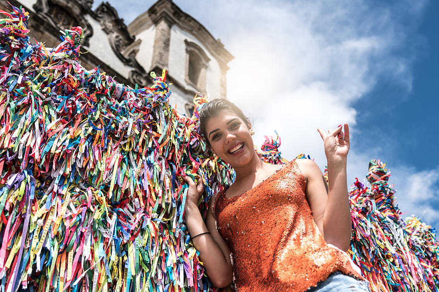 Woman making a wish with brazilian ribbons on church fence in Salvador, Bahia, Brazil Photograph by FG Trade