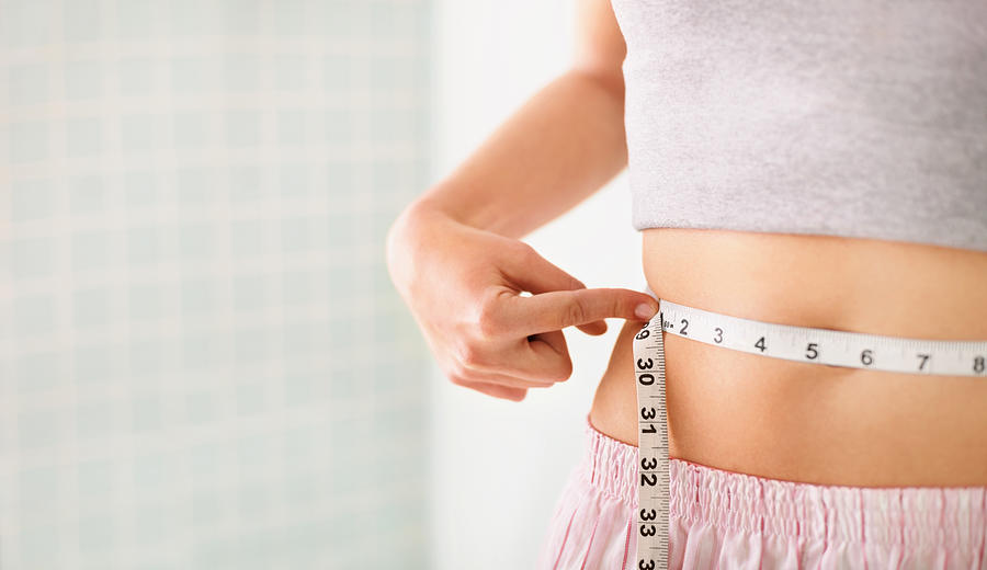 Woman measuring her waist over white Photograph by GlobalStock