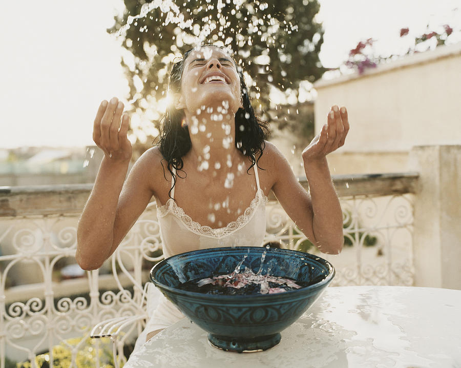 Woman on a Balcony Sits With Her Eyes Close, Splashing Water From a Bowl Photograph by Digital Vision.