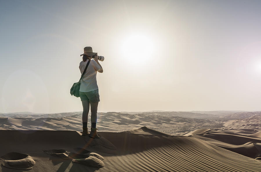 Woman on a sand dune taking pictures of sunset Photograph by Buena Vista Images