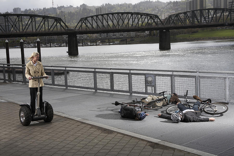 Woman on segway riding past two men and woman with bicycles lying on pavement by river Photograph by Kim Carson
