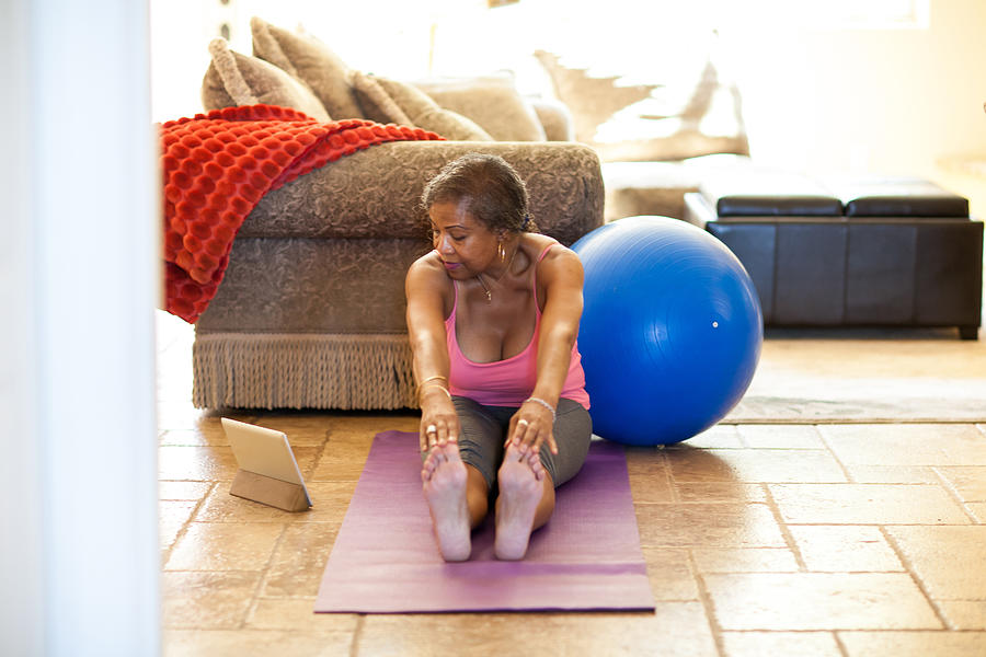 Woman on yoga mat using digital tablet, stretching Photograph by Deborah Kolb