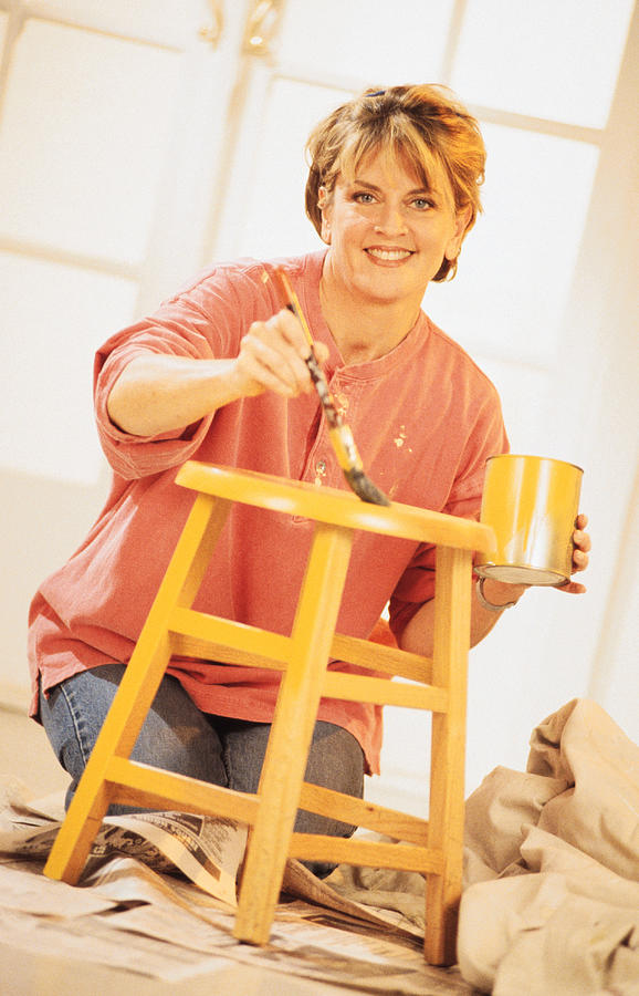 Woman painting stool at home Photograph by Comstock
