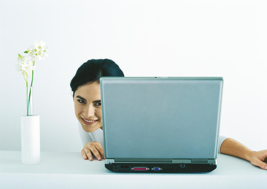 Woman peeking around side of laptop Photograph by Laurence Mouton