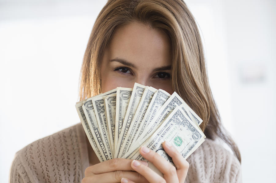 Woman peeking behind money Photograph by Jamie Grill