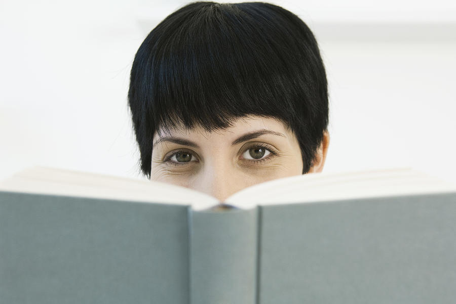 Woman peering over book at camera Photograph by ZenShui/Odilon Dimier