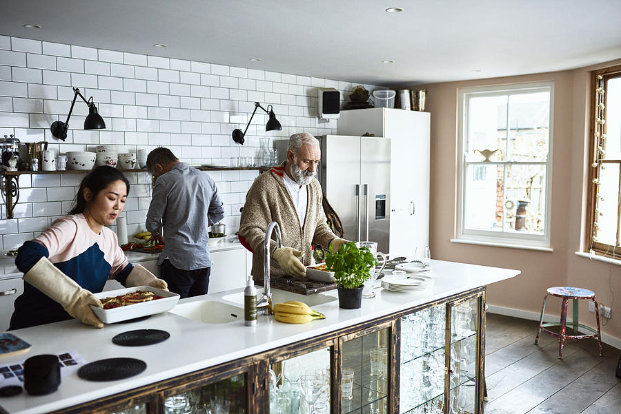 Woman placing hot lasagne dish on counter with father in law in kitchen Photograph by 10000 Hours