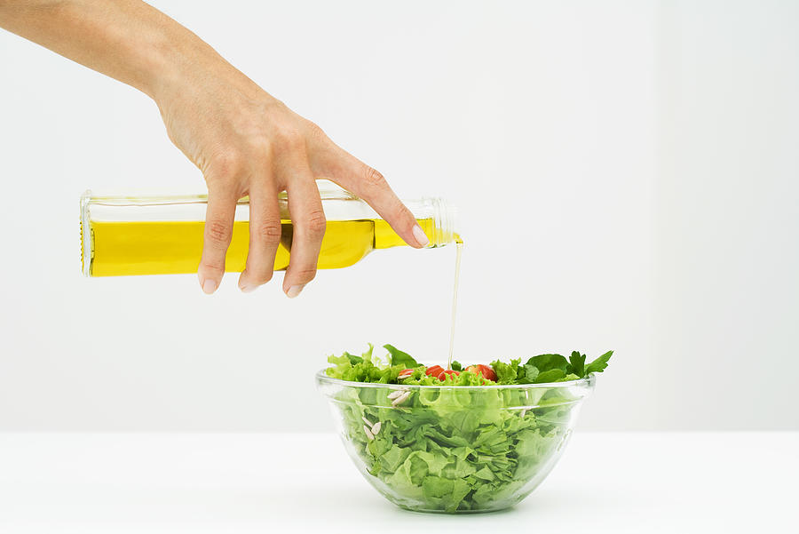 Woman pouring olive oil on salad, cropped view of hand Photograph by PhotoAlto/Laurence Mouton