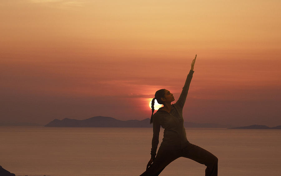 Woman practicing yoga against sunset Photograph by Tom Merton
