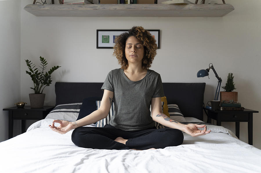 Woman practicing yoga, sitting on bed, meditating Photograph by Westend61