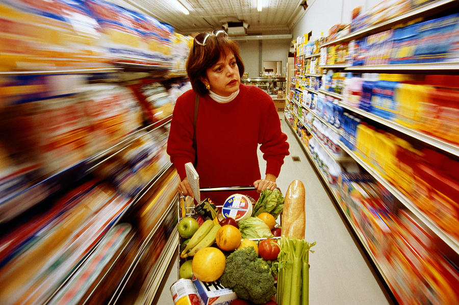 Woman pushing trolley in supermarket aisle (blurred motion) Photograph by Andy Sacks