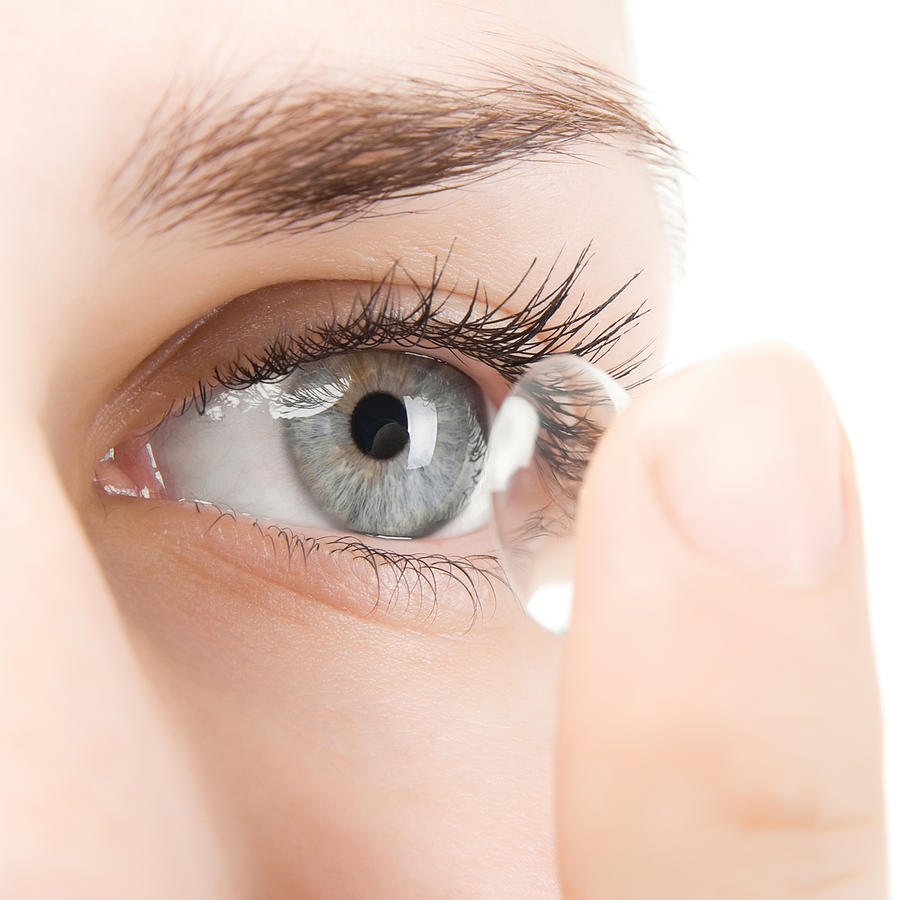 Woman putting contact lens into eye Photograph by PhotoBeaM