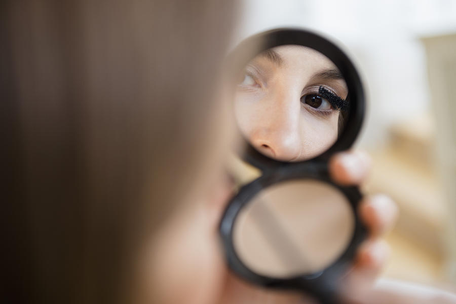 Woman putting on mascara in compact mirror Photograph by Jamie Grill