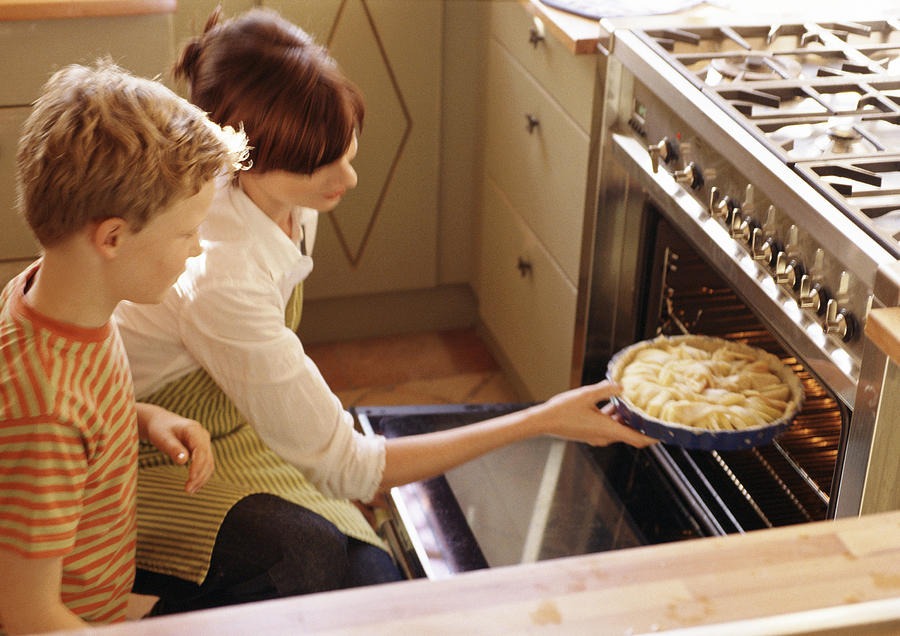 Woman putting pie in oven Photograph by Francis Hammond