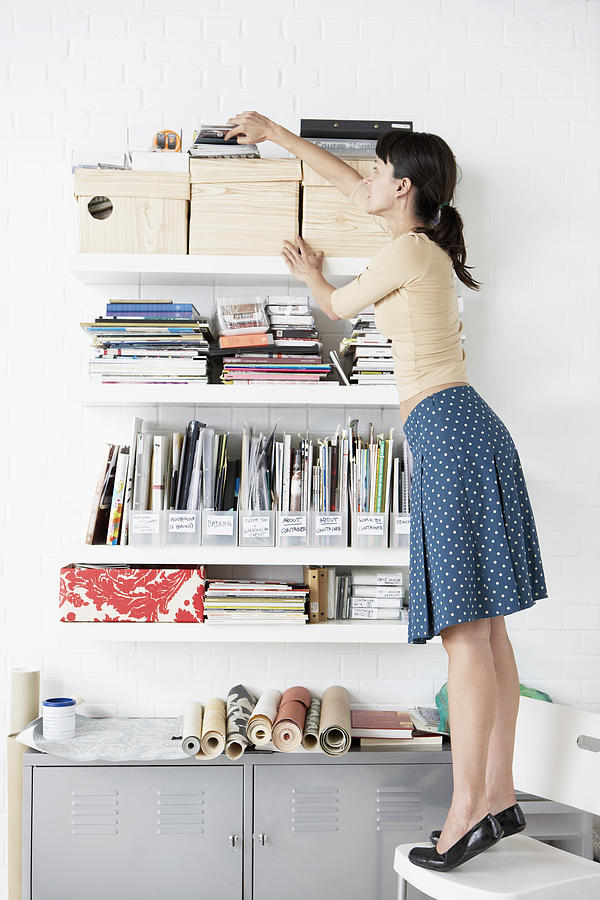 Woman Reaching for Shelf Photograph by Moodboard