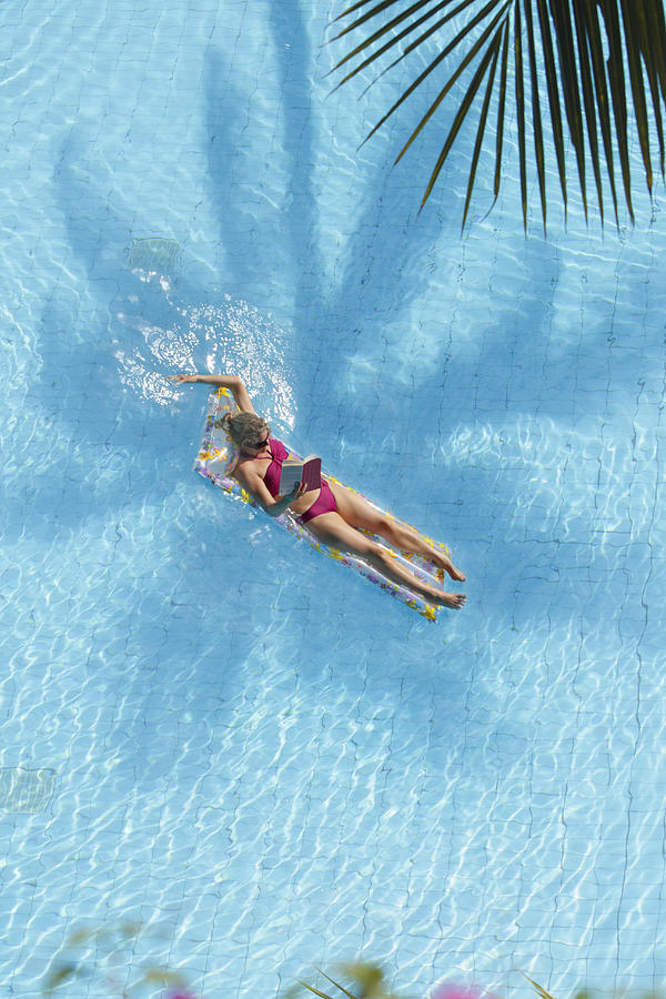 Woman Reading A Book On Lilo In Pool Photograph by Peter Cade