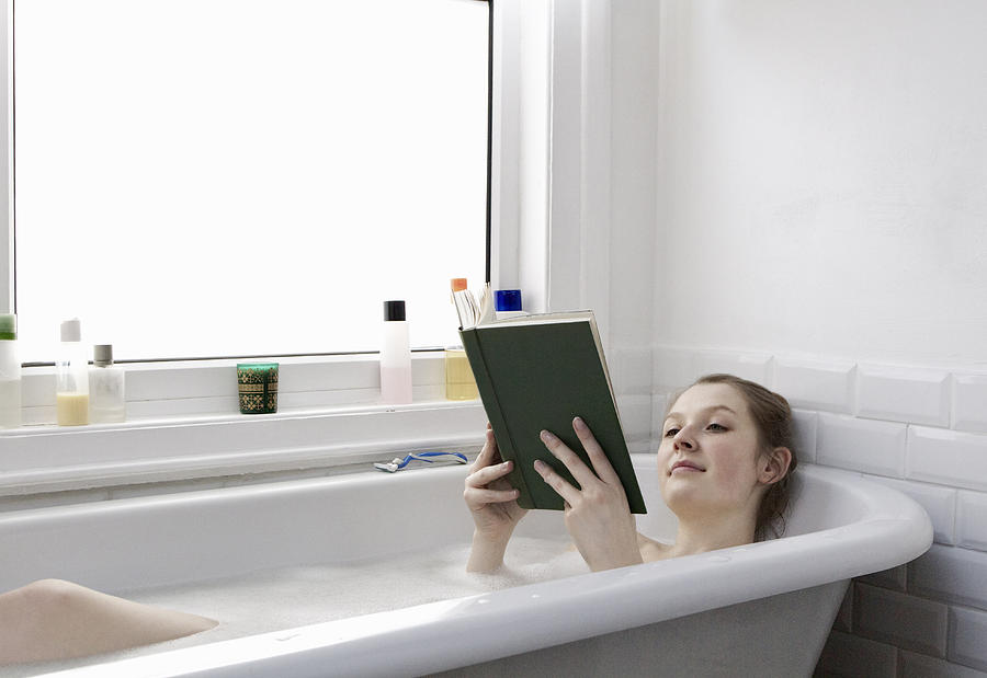 Woman relaxing at home reading a book in the bath Photograph by Flashpop