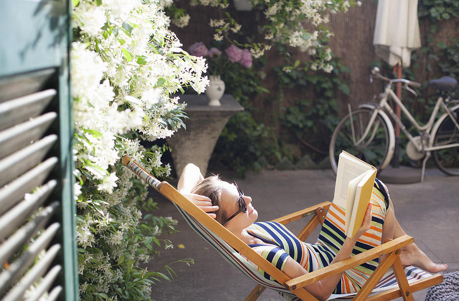 Woman relaxing on deck chair in backyard, reading a book Photograph by Kathrin Ziegler