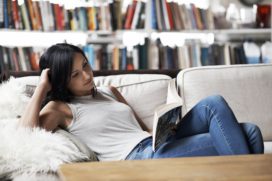 Woman relaxing on sofa reading a book Photograph by Morsa Images
