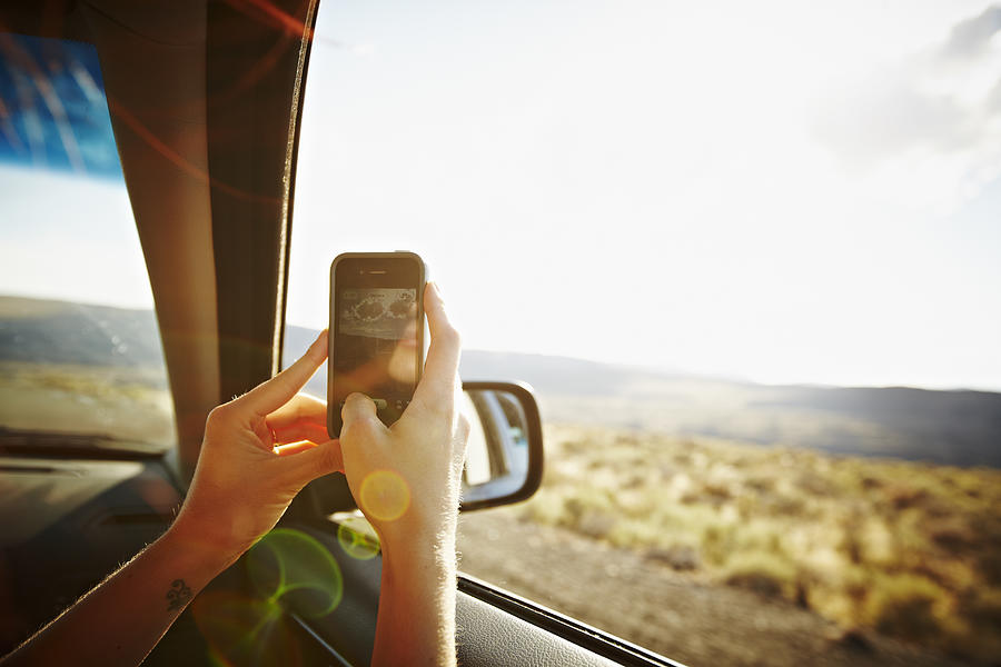 Woman riding in car taking photo with smartphone Photograph by Thomas Barwick