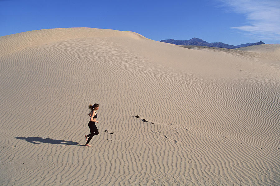 Woman running across sand dunes , Death Valley , California Photograph by Comstock