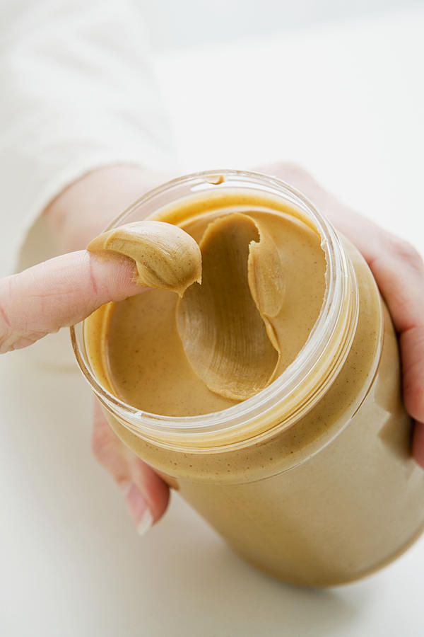 Woman scooping peanut butter from jar Photograph by Image Source